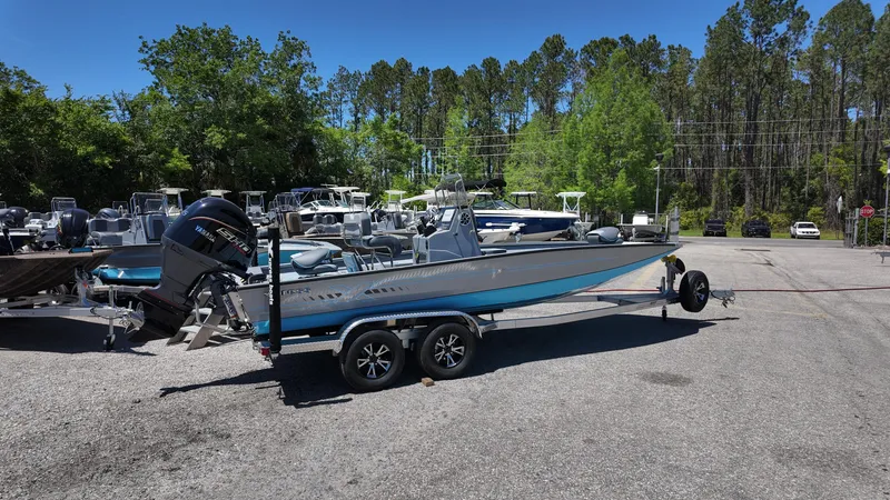 Slide: The Image of 2025 Xpress H22B boat on trailer in outdoor lot, surrounded by trees and other boats. - 13