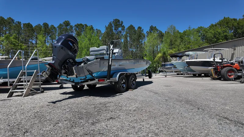 Slide: The Image of 2025 Xpress H22B boat on trailer in outdoor storage area with trees and blue sky. - 18