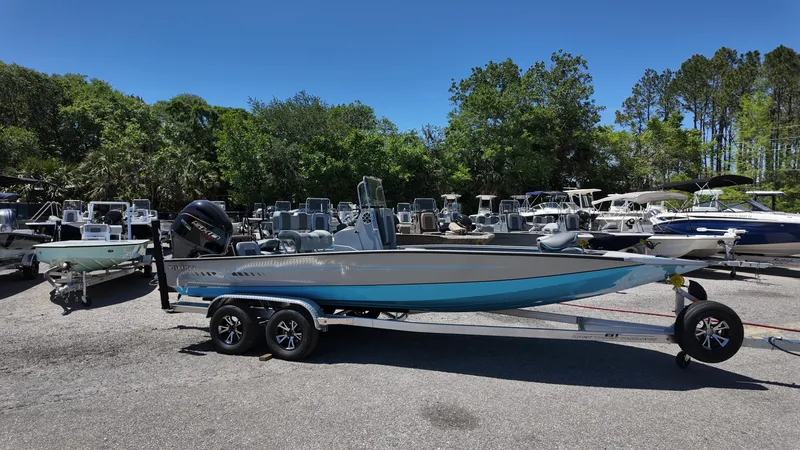 Slide: The Image of 2025 Xpress H22B boat on trailer in outdoor lot, surrounded by trees and other boats. - 7