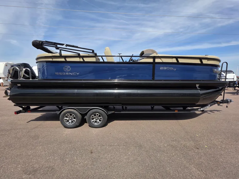 Slide: The Image of 2025 Regency 230 DL3 pontoon boat on trailer, side view, blue and black design. - 0