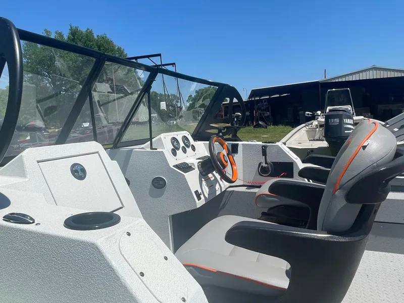 Slide: The Image of 2022 SeaArk ProCat 240 boat interior with steering wheel and seating, under clear blue sky. - 4