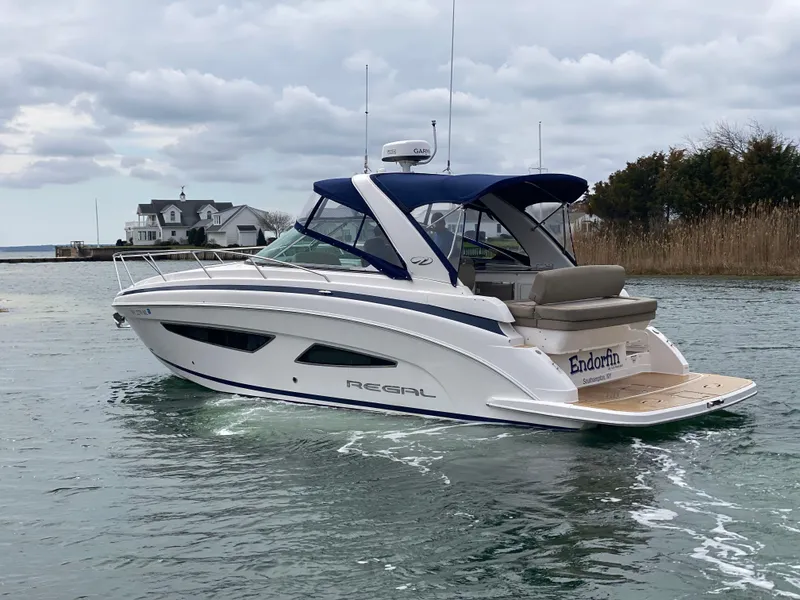 The Image of 2015 Regal 32 Express boat cruising on a calm waterway under cloudy skies. - 1