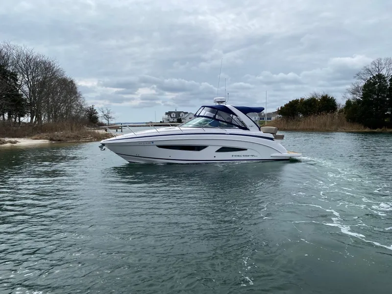 Slide: The Image of 2015 Regal 32 Express boat cruising on a calm waterway under cloudy skies. - 2