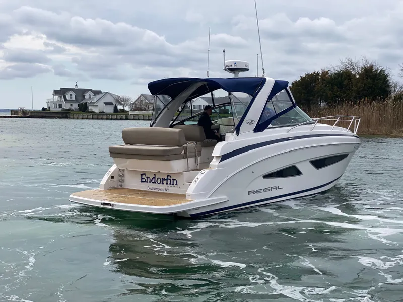 Slide: The Image of 2015 Regal 32 Express boat cruising on a calm waterway near a coastal house. - 9