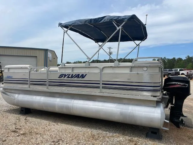 Slide: The Image of 1999 Sylvan 20 Elite pontoon boat with canopy, parked on gravel near a storage building. - 5