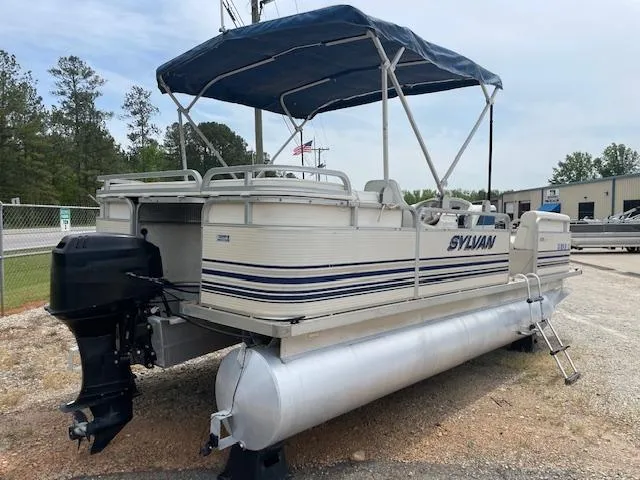 Slide: The Image of 1999 Sylvan 20 Elite pontoon boat with canopy, parked on gravel near trees and buildings. - 6