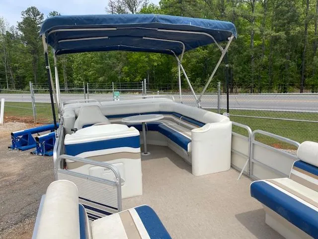 Slide: The Image of 1999 Sylvan 20 Elite pontoon boat with blue and white seating, parked near a road. - 7