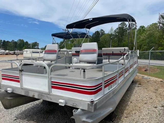 Slide: The Image of 1992 Leisure Island pontoon boat with canopy, parked on gravel, surrounded by trees and fencing. - 3