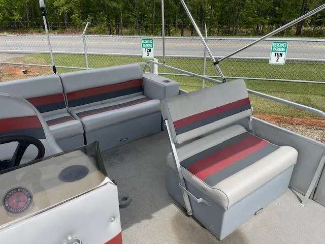 Slide: The Image of 1992 Leisure Island boat interior with gray and red seating, parked near a fence. - 8