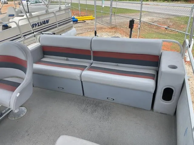 Slide: The Image of 1992 Leisure Island boat interior with gray and red seating, docked near a fence. - 9
