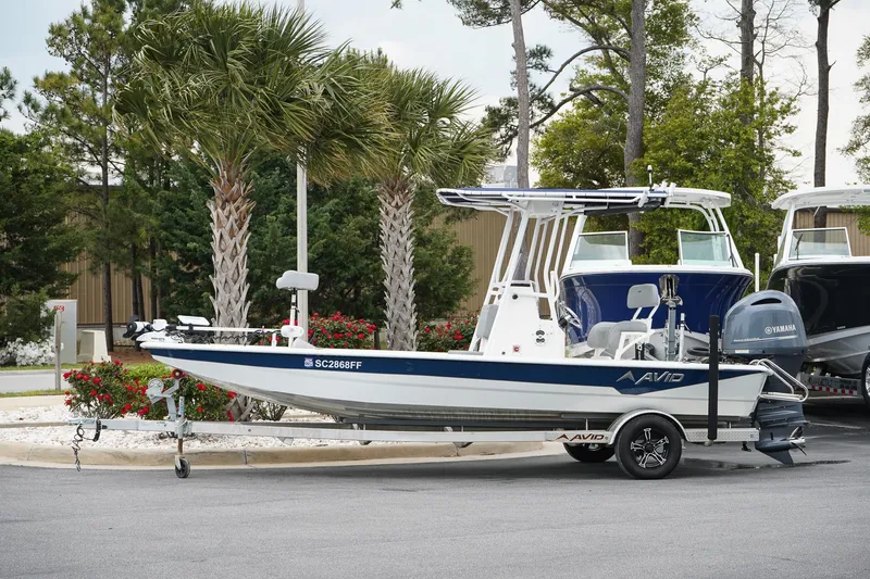 Slide: The Image of Avid 21 FS 2022 boat on trailer, parked near palm trees. - 1