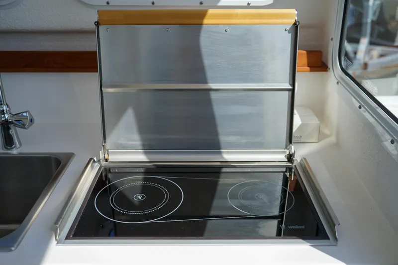 Slide: The Image of 2022 C-Dory 22' Cruiser kitchen with sleek induction cooktop and stainless steel backsplash. - 15