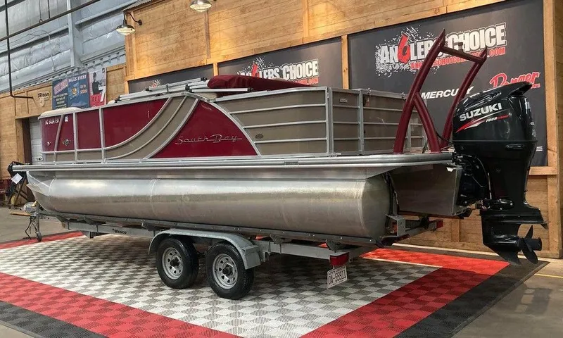 Slide: The Image of 2016 South Bay 521 FCR pontoon boat on trailer, displayed indoors with Suzuki outboard motor. - 3