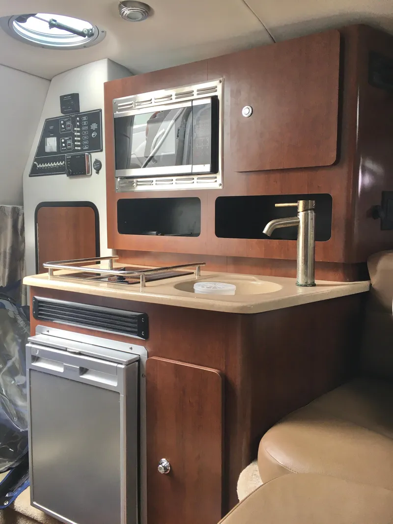 Slide: The Image of 2018 Crownline 264 CR boat interior with kitchenette, featuring microwave, sink, and compact fridge. - 21