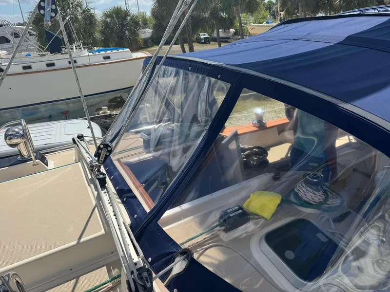 Slide: The Image of 2002 Island Packet 380 sailboat cockpit with blue canopy and clear windows, docked near palm trees. - 5