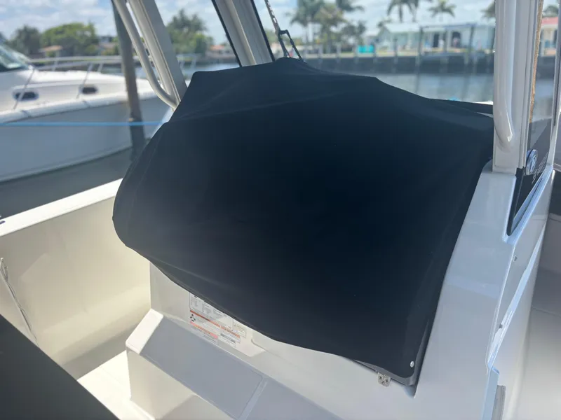 Slide: The Image of 2022 Pursuit S 288 boat console covered, docked near water with palm trees in background. - 17