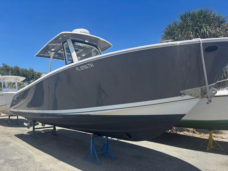 Slide: The Image of 2022 Pursuit S 288 boat on stands, gray hull, sunny day, palm trees in background. - 30