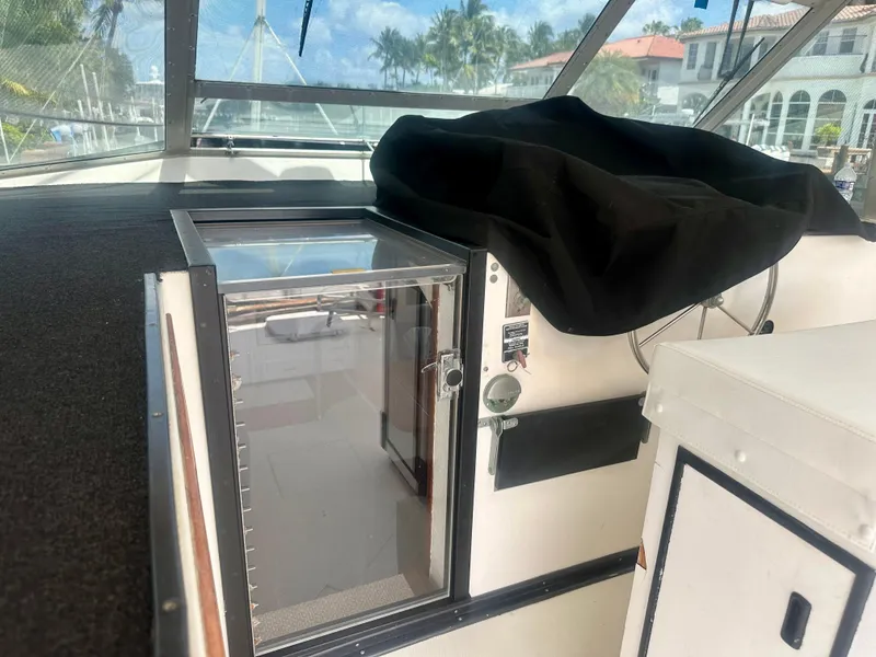 Slide: The Image of 1974 Bertram 42 Motor Yacht cockpit with covered controls and clear hatch, docked near luxury homes. - 19