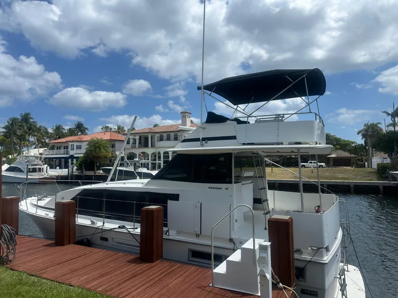 Slide: The Image of 1974 Bertram 42 Motor Yacht docked by waterfront homes under a partly cloudy sky. - 3