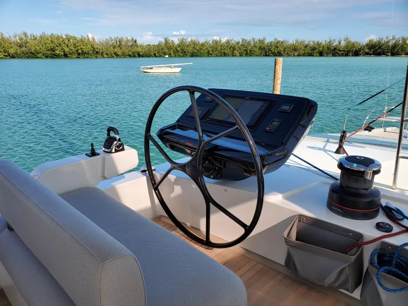 Slide: The Image of Helm of 2020 Lagoon SEVENTY 7 yacht with serene water backdrop. - 2