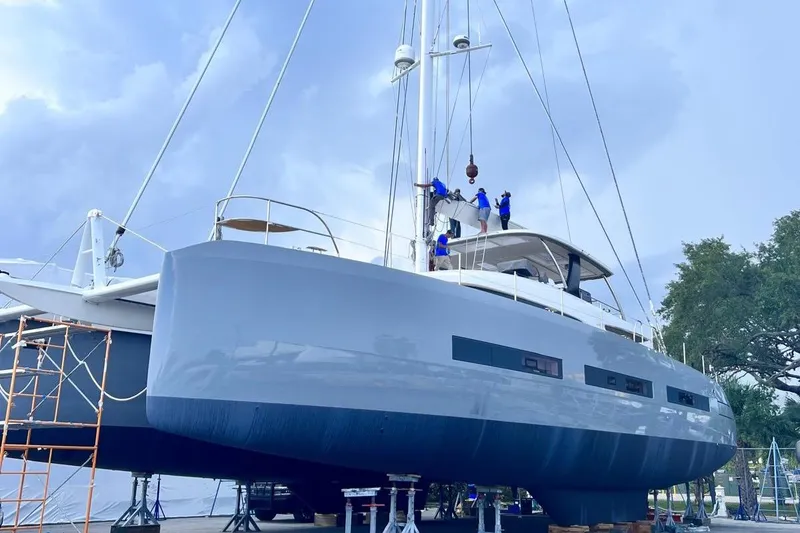 Slide: The Image of 2020 Lagoon SEVENTY 7 yacht on dry dock with workers, under a cloudy sky. - 45