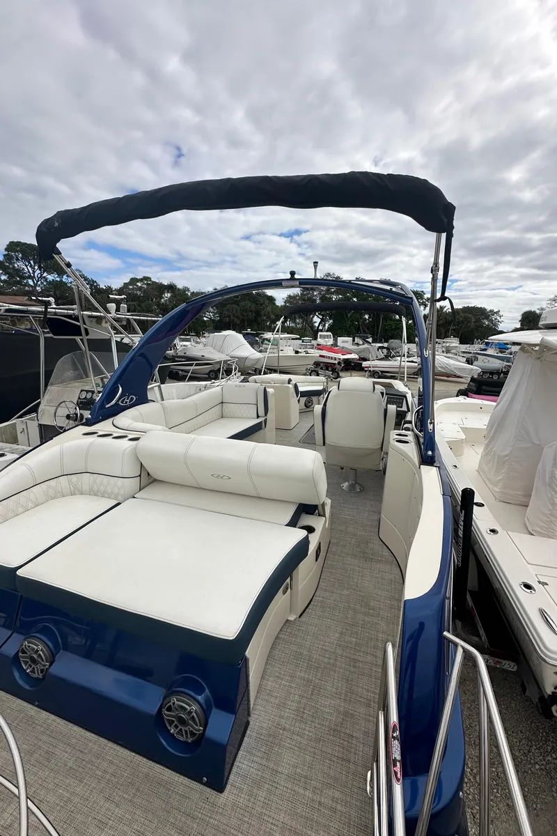 Slide: The Image of 2022 Harris Crowne SL 250 pontoon boat with white seating and blue exterior, docked under cloudy skies. - 4