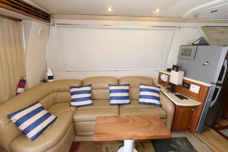 Slide: The Image of 1999 Carver 450 Voyager Pilothouse interior with beige sofa, striped pillows, and compact kitchen area. - 10