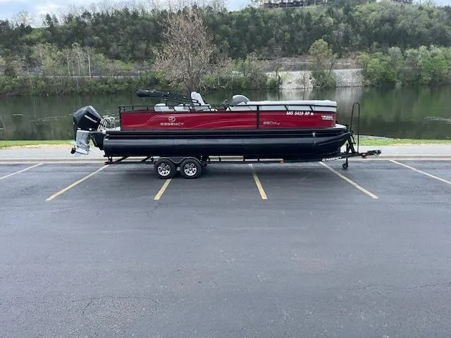 Slide: The Image of 2024 Regency 250 DL3 pontoon boat on trailer, parked by a scenic lake. - 9