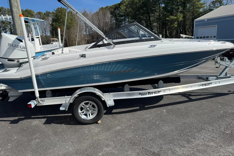 Slide: The Image of 2025 Stingray 191 DC boat on trailer, parked outdoors near trees and buildings. - 6