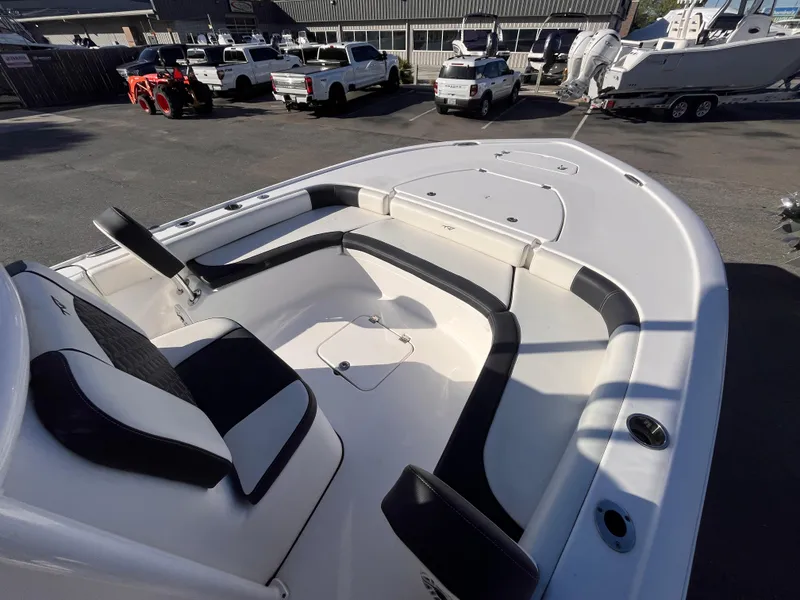 Slide: The Image of 2021 Tidewater 2500 Carolina Bay boat interior with seating and storage, parked among vehicles. - 10