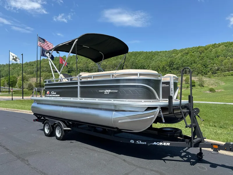 Slide: The Image of 2025 Sun Tracker Party Barge 20 DLX pontoon boat on trailer, parked outdoors. - 2
