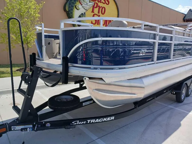 Slide: The Image of 2025 Sun Tracker Fishin' Barge 20 DLX pontoon boat on trailer, parked outside. - 2