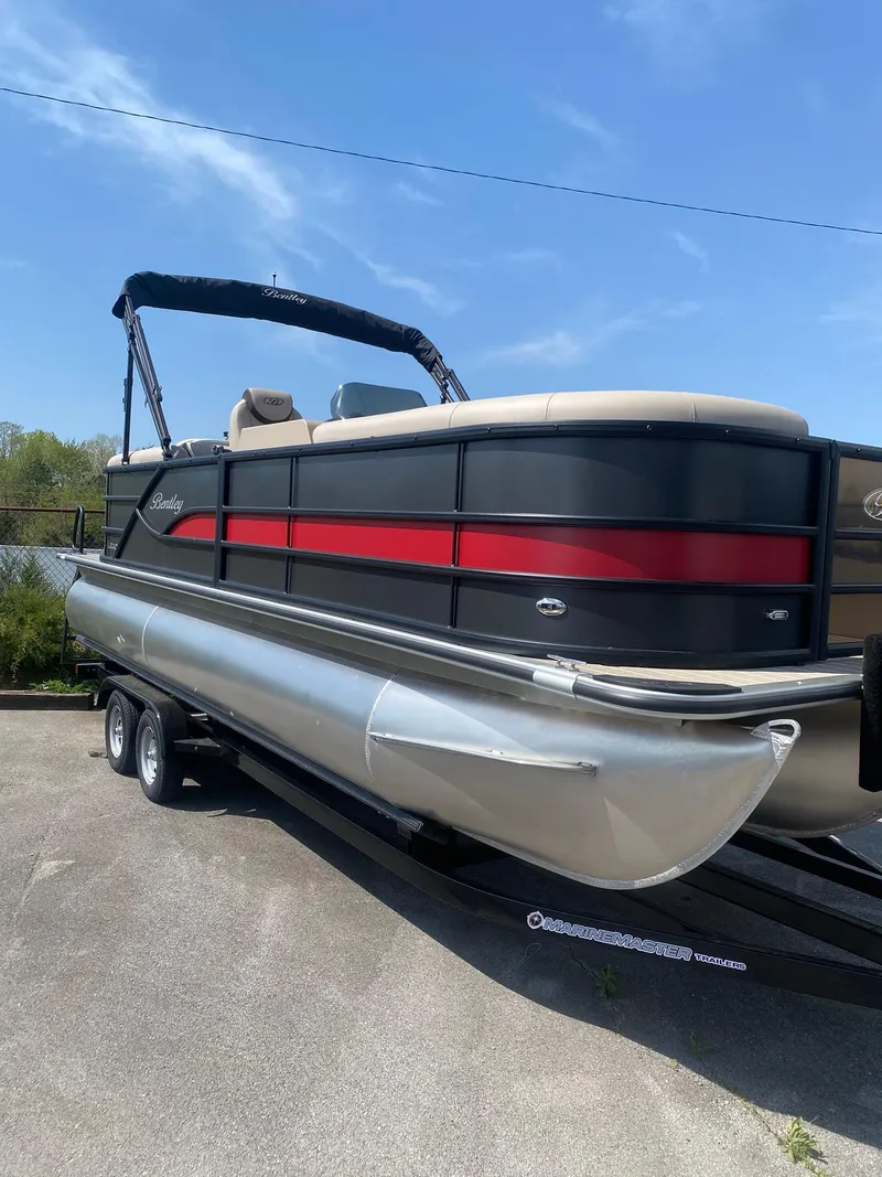 Slide: The Image of 2025 Bentley Pontoons Legacy 223 Navigator on trailer, sleek design with red accent, under clear sky. - 14