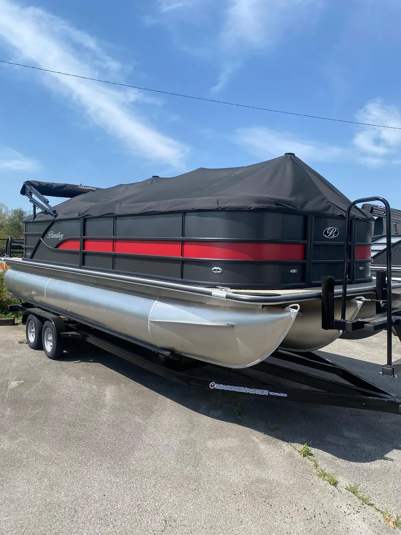 Slide: The Image of 2025 Bentley Pontoons Legacy 223 Navigator on trailer, covered, under clear blue sky. - 6