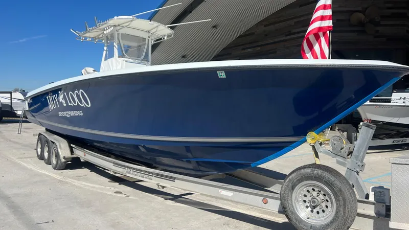 Slide: The Image of 2005 Contender 36 boat on trailer with American flag, blue hull, docked outdoors. - 1