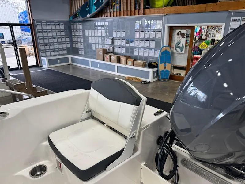 Slide: The Image of 2025 Robalo R160 Center Console boat seat in a showroom with surfboards and accessories. - 6