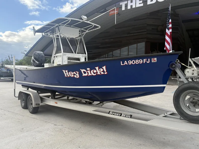 Slide: The Image of Blue Skiff Reno 23 boat on trailer, labeled "Hey Dick!", parked outside a building. - 3