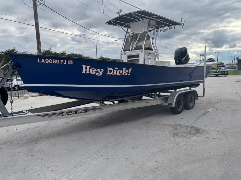 Slide: The Image of Blue Skiff Reno 23 boat on trailer, labeled "Hey Dick!", overcast sky. - 4