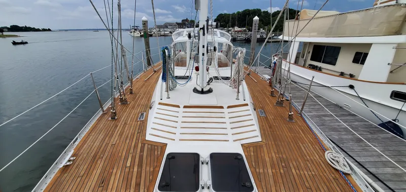 Slide: The Image of 1989 Tayana 55 sailboat with teak deck, docked at a marina, surrounded by calm waters. - 11