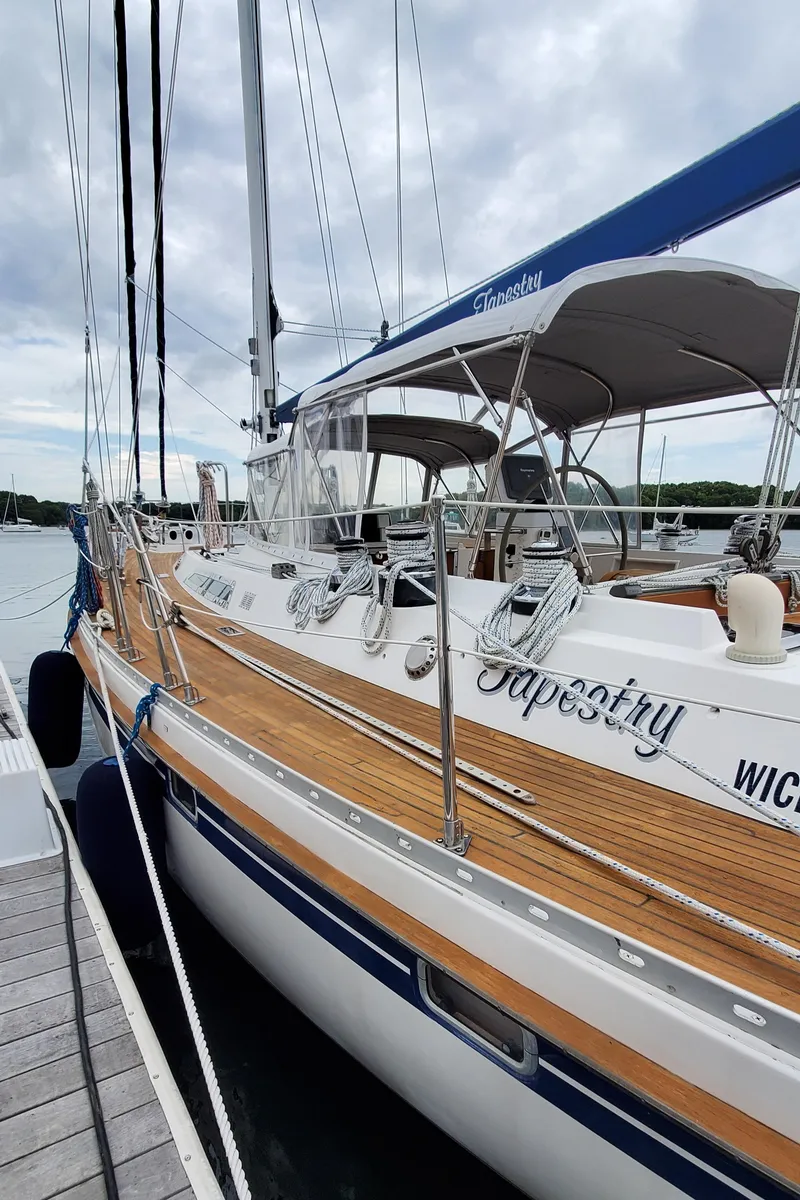 Slide: The Image of 1989 Tayana 55 sailboat docked, featuring teak deck and blue accents under cloudy sky. - 6