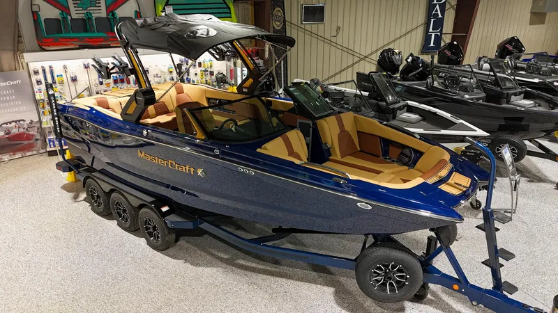 Slide: The Image of 2025 MasterCraft X24 boat in showroom, blue exterior, tan interior, on trailer. - 1