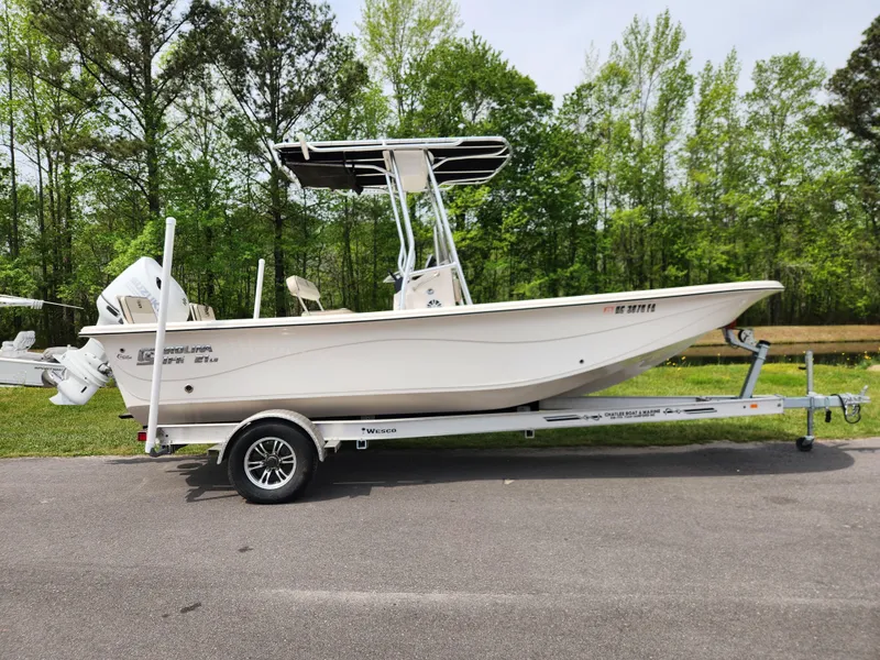 Slide: The Image of 2023 Carolina Skiff 21 LS boat on trailer, parked outdoors with trees in background. - 0