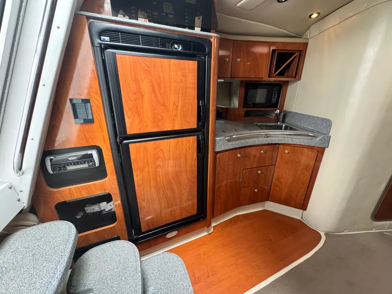 Slide: The Image of 2005 Larson 370 Cabrio interior with kitchenette, featuring wood cabinetry, fridge, and microwave. - 18