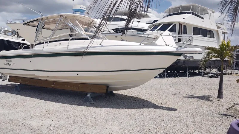 Slide: The Image of 2005 Intrepid 310 Walkaround boat on gravel lot, surrounded by palm trees and other boats. - 6