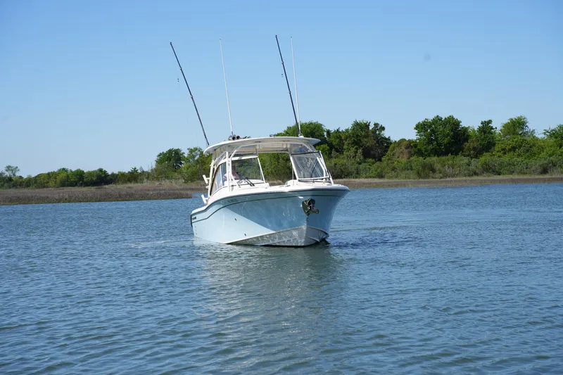 Slide: The Image of 2022 Grady-White Freedom 285 boat on calm water, clear sky, lush greenery. - 6