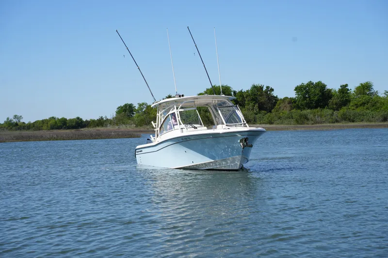 Slide: The Image of 2022 Grady-White Freedom 285 boat on calm water, clear sky, lush greenery background. - 7