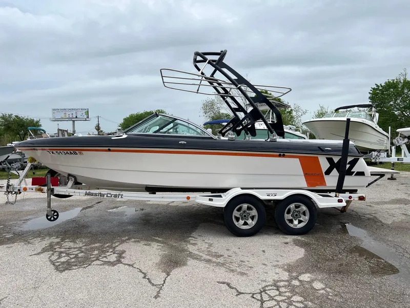 Slide: The Image of 2006 MasterCraft X1 boat on trailer, white with orange accents, parked outdoors. - 2