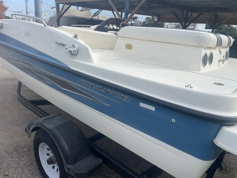 Slide: The Image of 2011 Bayliner 197 boat on trailer, blue and white exterior, parked under shelter. - 2