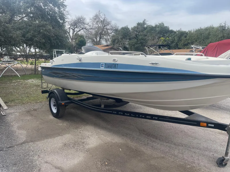 Slide: The Image of 2011 Bayliner 197 boat on trailer, parked outdoors, surrounded by trees and other boats. - 5