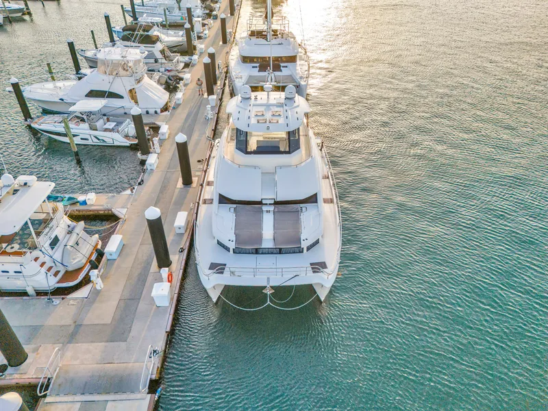 Slide: The Image of 2023 Aquila 54 Yacht docked in a scenic waterfront setting with palm trees. - 107